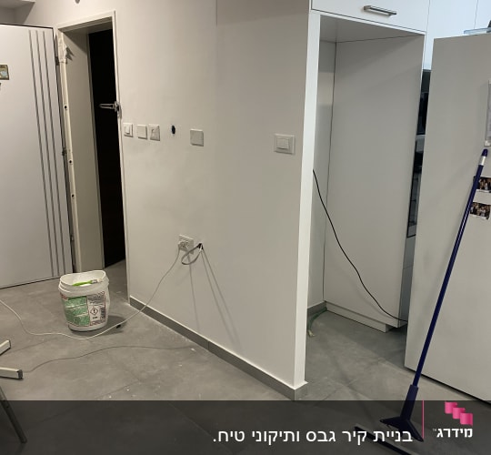 קיר גבס עם דלי צבע ומגב על הרצפה
